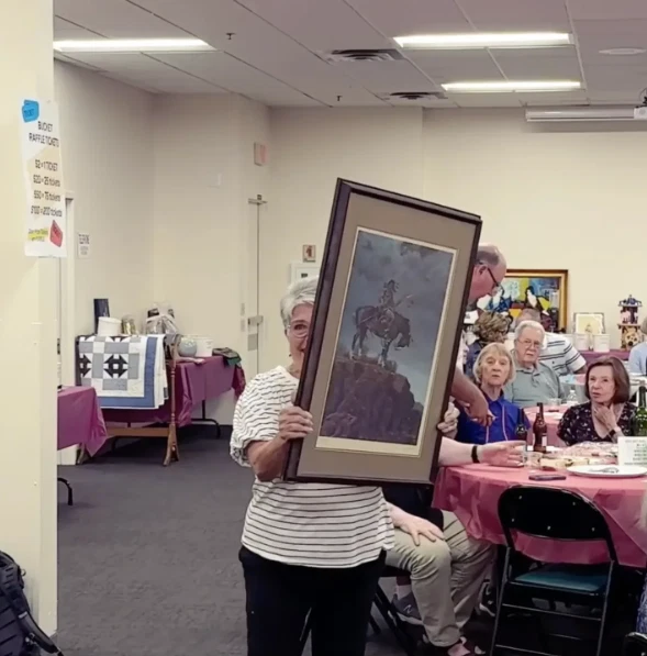 Resident displaying a framed artwork donation at a Sun City West Foundation An Artistic Affair preview gathering.