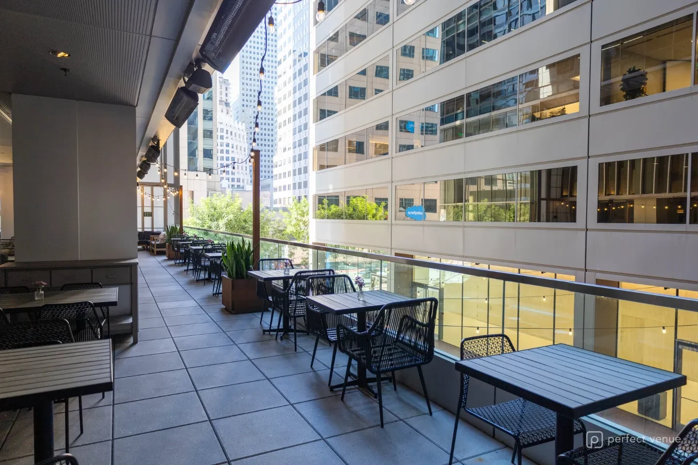 Outdoor terrace seating with black bistro tables and chairs overlooking a downtown skyline of glass office towers.