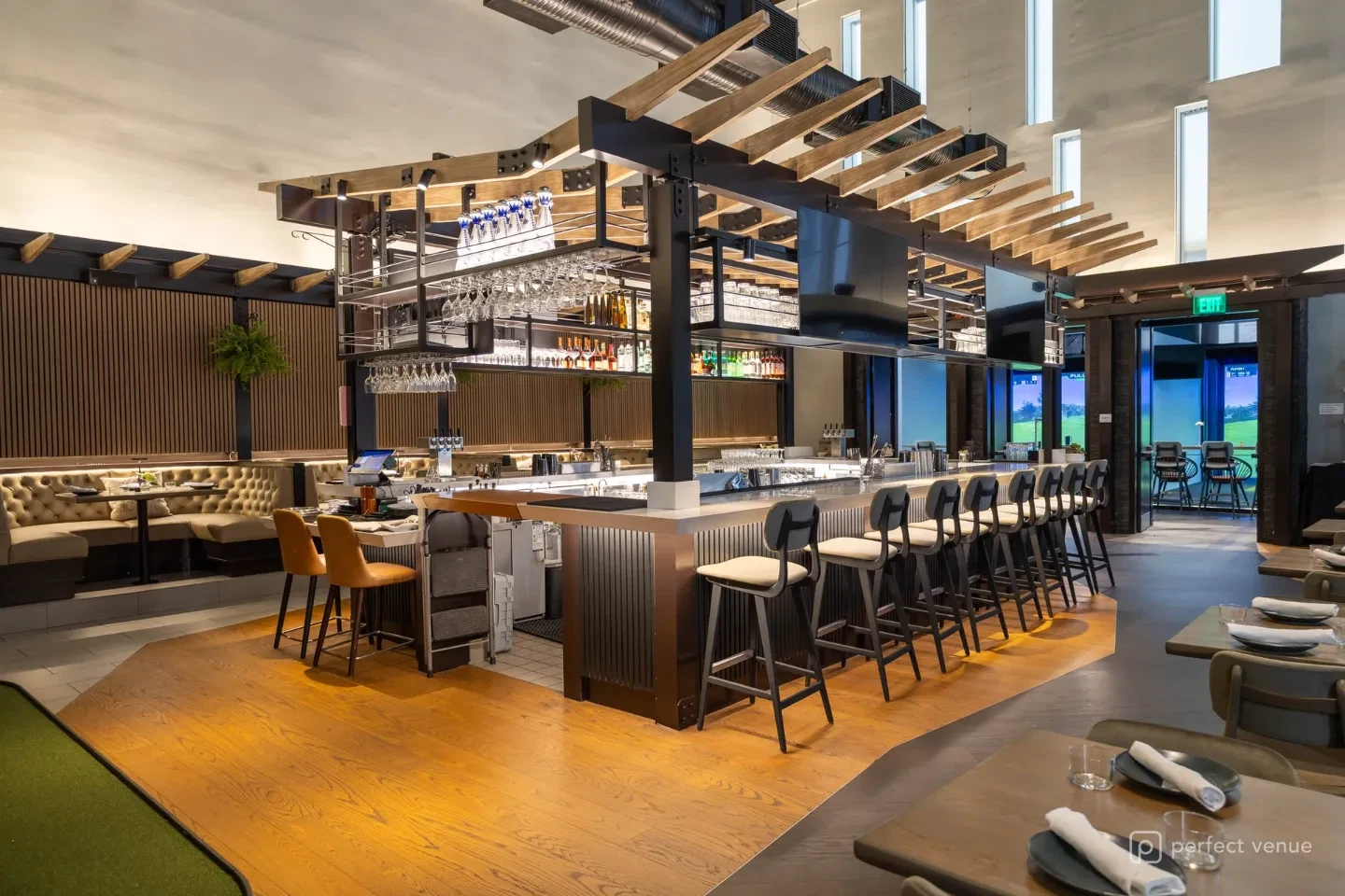 Modern restaurant bar with a suspended wood-slat canopy, hanging stemware racks, leather banquette booths, and a long row of upholstered bar stools.