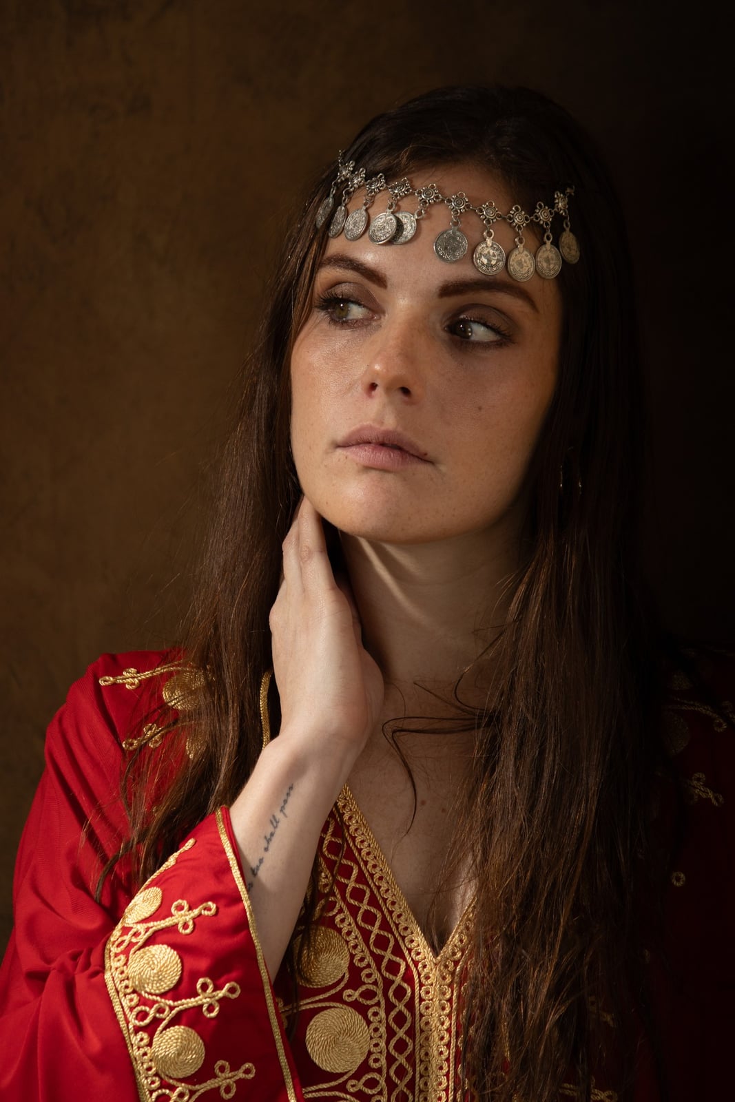 From the Maison Maure series: portrait of a woman in an embroidered red jacket, hand raised to her neck, against a dark ground.